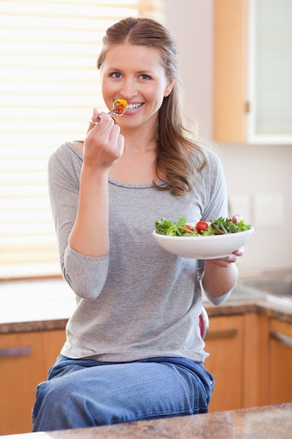 Femme mangeant de la salade dans la cuisine