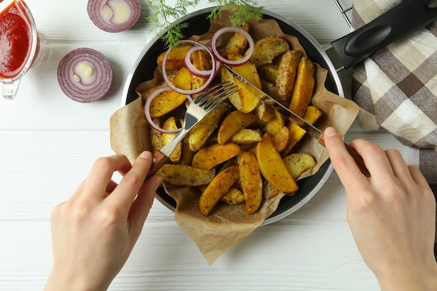 Femme mangeant de savoureuses pommes de terre au four sur table en bois blanc, vue du dessus