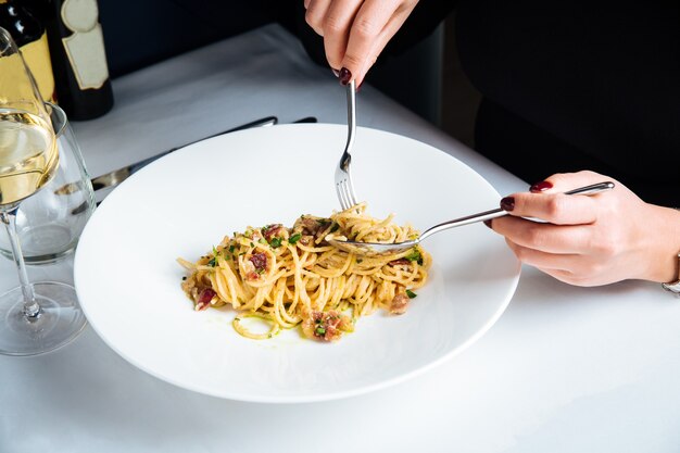 Femme mangeant des spaghettis italiens carbonara avec du vin blanc