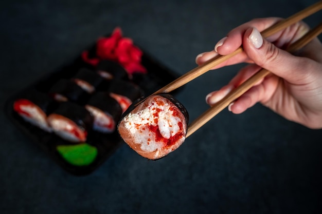 Femme mangeant des sushis livrés dans un conteneur avec des bâtons japonais