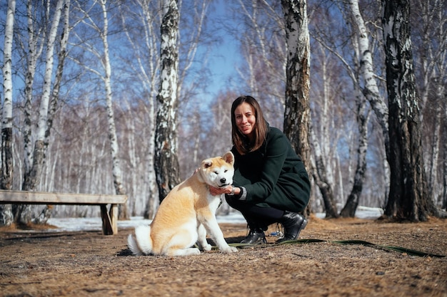 Femme en manteau et un chiot akita inu dans un parc de bouleaux d'hiver regardez la caméra