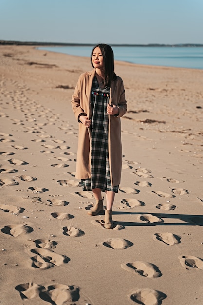 Femme en manteau marchant sur la plage de sable à Angelholm, Suède