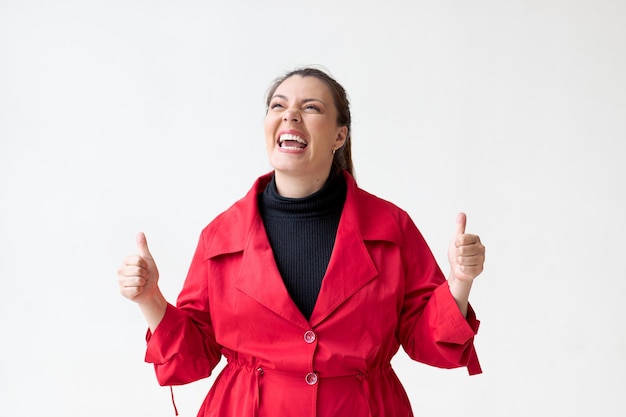 Photo femme en manteau rouge sur fond blanc sourit avec les pouces vers le haut