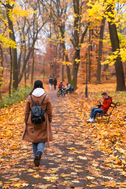 Photo femme en manteau avec sac à dos marchant dans le parc de la ville d'automne