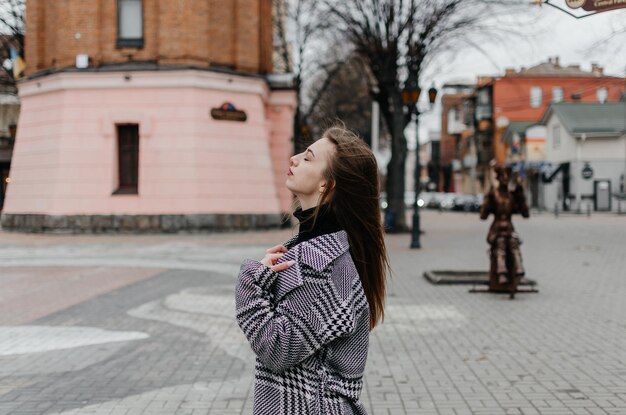 Une femme en manteau se tient dans la rue devant un bâtiment rose