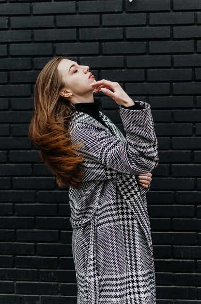 Une femme en manteau se tient devant un mur de briques noires