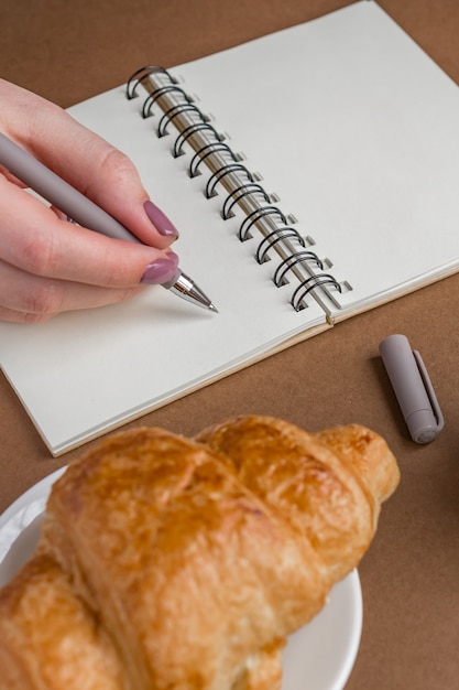 Femme avec manucure écrit sur ordinateur portable. Pigiste travaillant à l'extérieur. Croissant savoureux sur une plaque blanche sur la table.