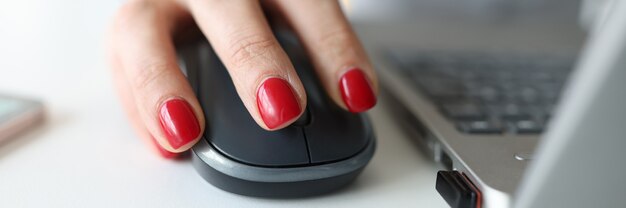 Femme avec manucure rouge tenant une souris d'ordinateur près d'un ordinateur portable en gros plan