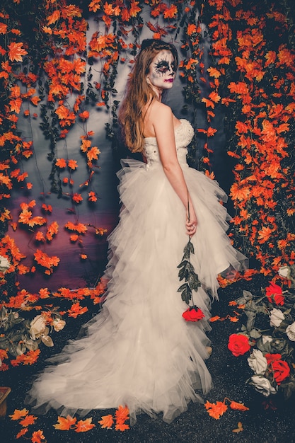 Femme avec maquillage fantôme et robe de mariée tenant un demi-côté rose.