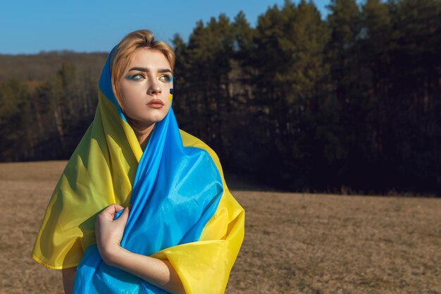 Femme avec un maquillage patriotique enveloppé dans un drapeau ukrainien Stand avec le concept de l'Ukraine