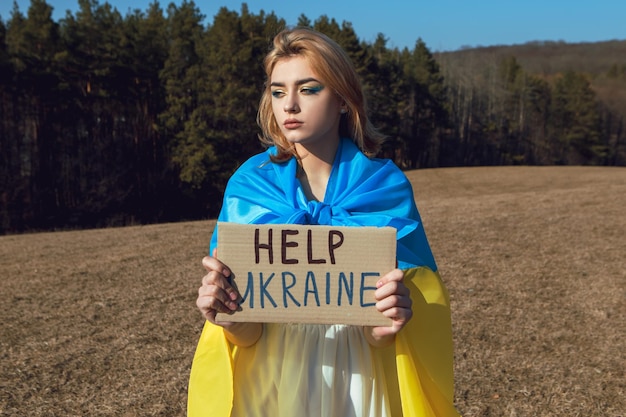 Photo femme avec un maquillage patriotique enveloppé dans un drapeau ukrainien tenir une pancarte de protestation stand avec le concept de l'ukraine