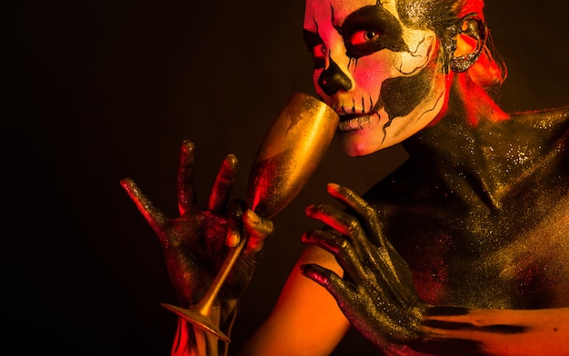 femme avec maquillage squelette tient le verre