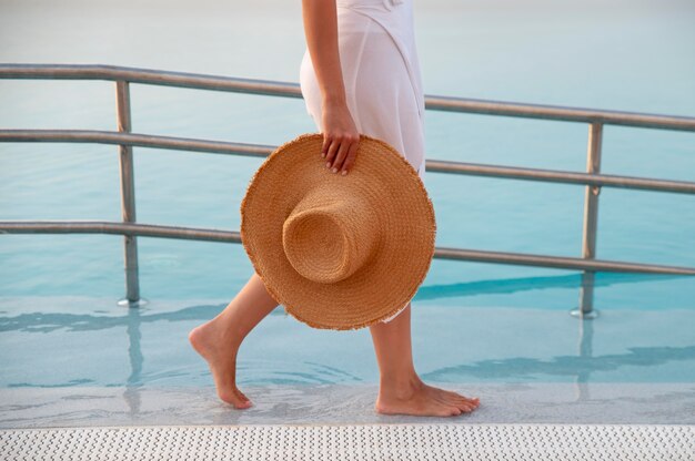 Photo femme marchant à côté d'une piscine tout en tenant son chapeau de paille