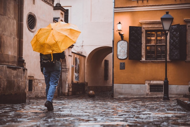 Femme marchant dans les vieilles rues européennes par temps de pluie avec espace de copie de parapluie jaune