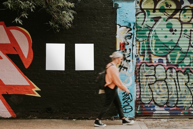 Femme marchant devant une peinture murale d'art de rue et des affiches vierges