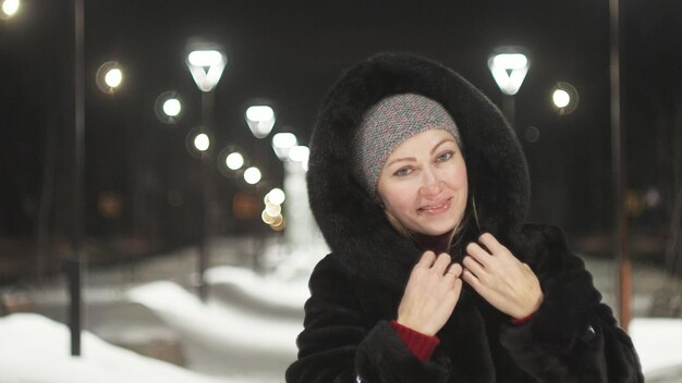 Femme marchant le long du manteau de fourrure noir Outdoor Girl marche une nuit d'hiver parmi les lampadaires