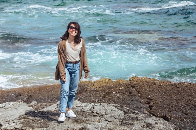 Femme marchant sur la plage de la mer rocheuse aux vacances d'été ensoleillées et venteuses