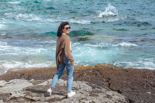 Femme marchant sur la plage de la mer rocheuse aux vacances d'été ensoleillées et venteuses