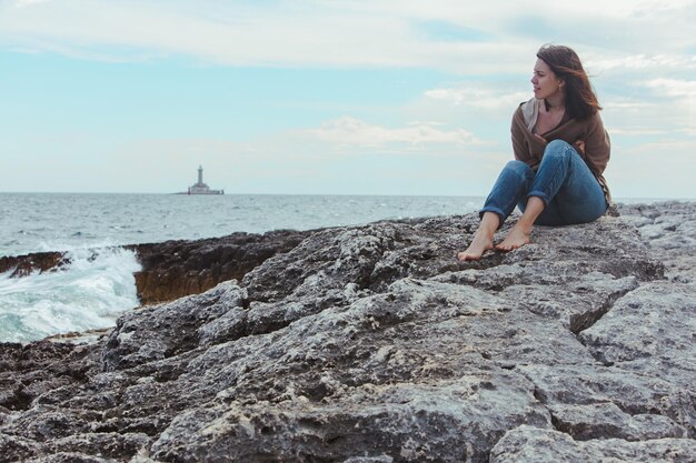 Femme marchant sur la plage rocheuse de la mer dans un phare de jeans mouillés sur fond