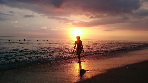 Femme marchant sur le rivage contre le ciel au coucher du soleil