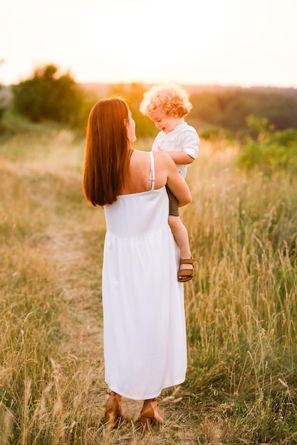 Femme marchant avec son fils le long d'un champ pittoresque au coucher du soleil