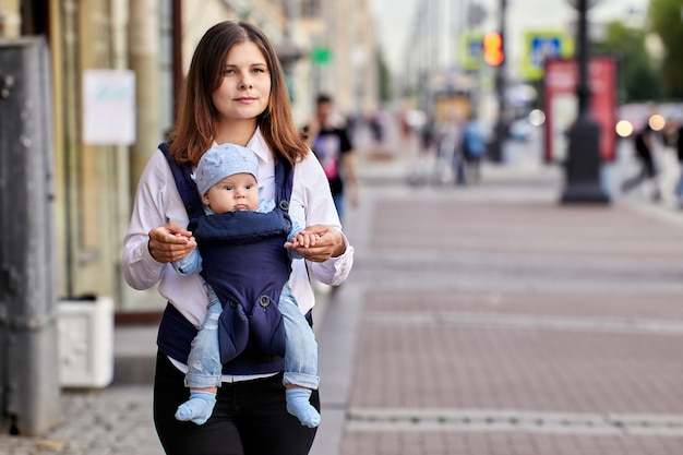 Femme marche avec bébé en écharpe dans une rue bondée