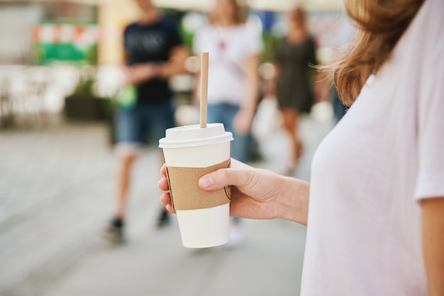 Une femme marche dans la rue de la ville avec une tasse de café en papier