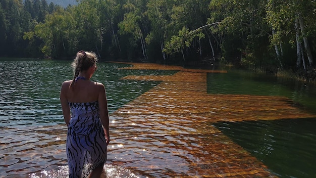 Femme marche sur l'eau sur la jetée dans des lunettes de soleil et un châle en soie boho Fille reste sur le quai sous-marin en bois d'inondation Le trottoir est recouvert d'eau dans le lac