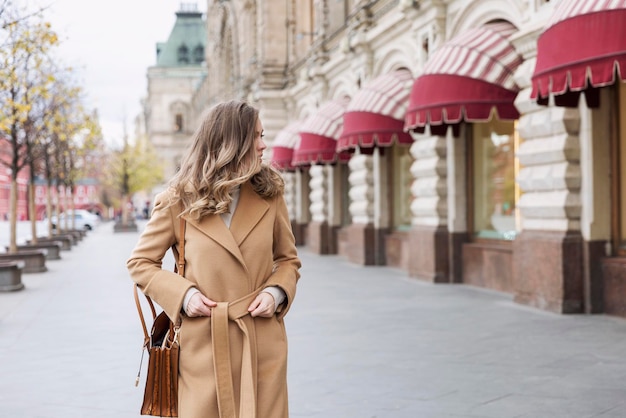 Une femme marche le long du Gum sur la Place Rouge et regarde les vitrines des magasins. Blonde élégante dans un manteau beige.