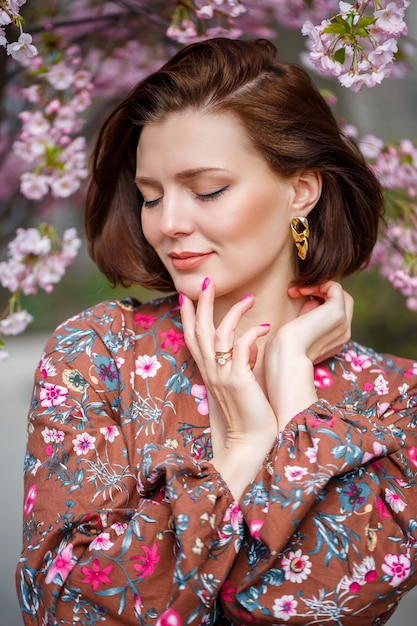 Une femme marche le long d'une rue printanière. La fille apprécie l'odeur d'un arbre en fleurs. Belle femme vêtue d'une robe avec sakura cerise en fleurs