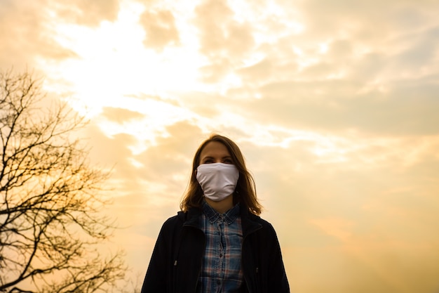 Photo la femme marche en masque dans la nature. protection contre le coronavirus. pas de monde autour. la fille garde la distance. beau ciel sur fond. arrêtez l'épidémie.