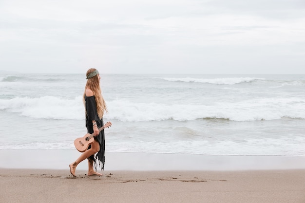 femme marche près de la mer avec ukulélé