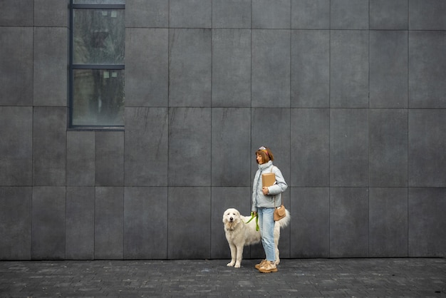 Femme marche avec son chien blanc sur fond de mur gris à l'extérieur