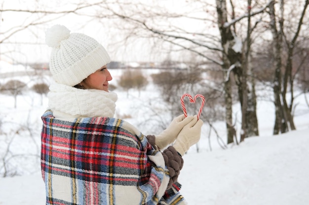 Une femme marche à travers la forêt d'hiver, elle tient des cannes de bonbon dans ses mains