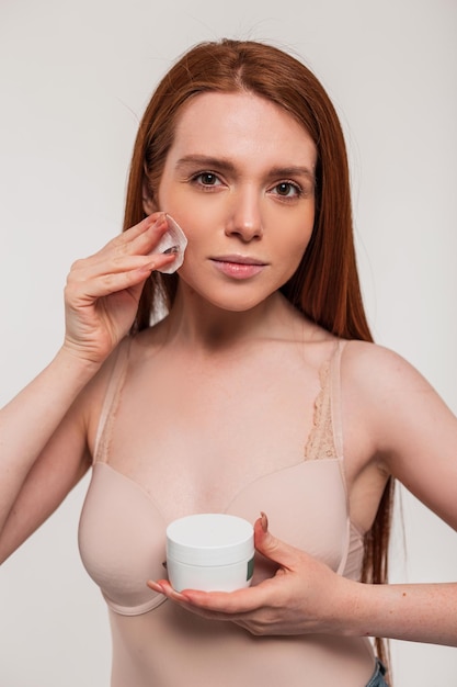 Une femme avec un masque blanc et une bouteille de crème pour le visage.