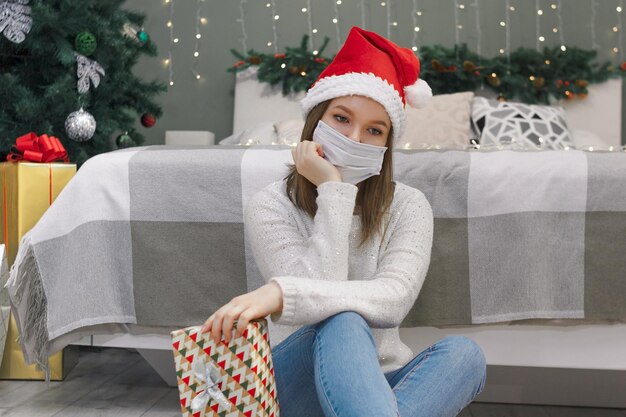 Femme avec un masque et un chapeau de Père Noël sur le sol avec une quarantaine de cadeaux ou une auto-isolation à Noël du Nouvel An