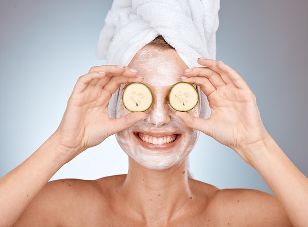 Femme masque de concombre et de soin de la peau pour la beauté, la santé et le bien-être par fond de studio avec sourire Masque crème et modèle avec des légumes pour le nettoyage du visage et des cosmétiques avec bonheur pour la peau