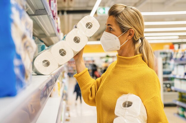 Femme avec masque facial faisant ses courses au supermarché achetant du papier toilette lors de la pandémie de coronavirus COVID-19