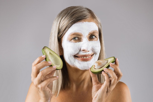 Femme avec masque facial en studio tenant des moitiés d'avocat