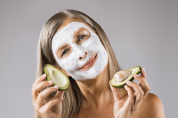 Femme avec masque facial tenant des moitiés d'avocat en studio