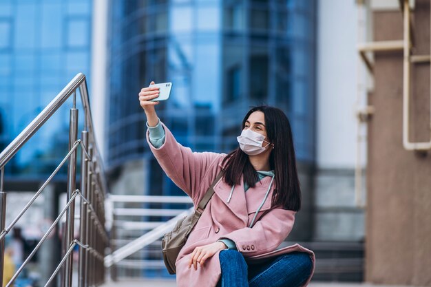 Femme en masque médical à l'extérieur à l'aide d'un téléphone intelligent. Protection de la santé et prévention des épidémies de virus grippal, coronavirus, COVID-19, épidémie et pandémie, maladies infectieuses, concept de quarantaine.