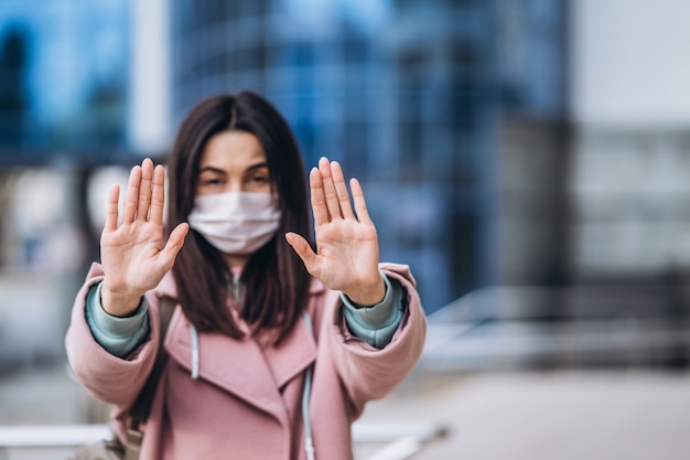 Femme en masque médical à l'extérieur montre un panneau d'arrêt par ses mains pour une distance de sécurité sociale afin de prévenir l'infection par le virus. Coronavirus, COVID-19, virus, maladie, épidémie, pandémie, concept de quarantaine.