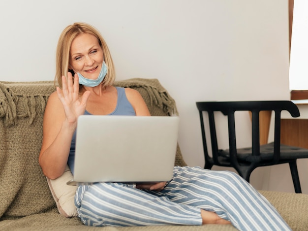 Photo femme avec masque médical et ordinateur portable à la maison pendant la quarantaine