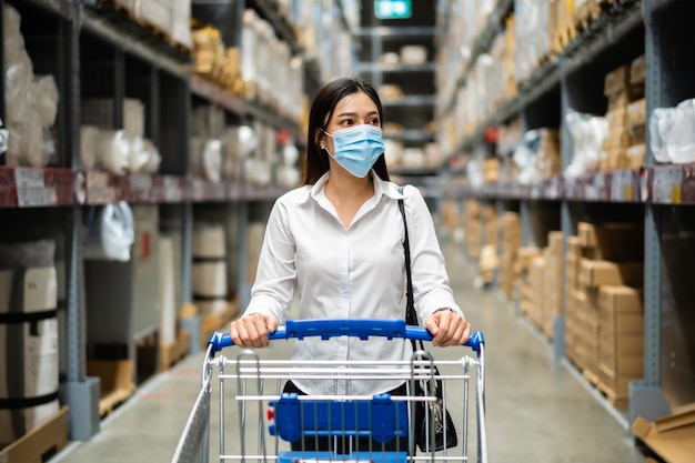 Femme avec masque médical à la recherche et faire du shopping dans le magasin de l'entrepôt pendant la pandémie de coronavirus