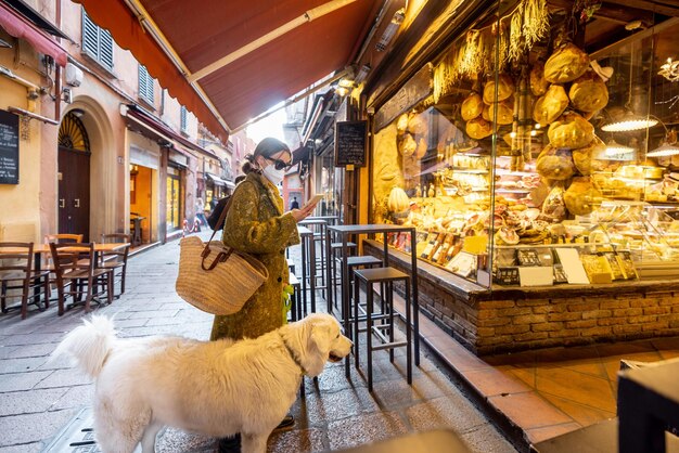 Femme en masque médical avec son chien près du magasin d'alimentation de la ville de bologne