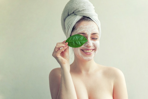 femme avec masque nourrissant blanc ou crème sur le visage et feuille verte à la main, fond blanc