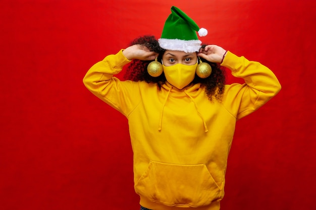 Femme avec masque de protection et bonnet de Noel a des sphères de décoration d'arbre de Noël dans ses mains