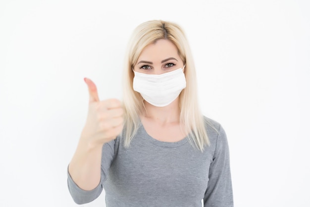 Femme avec masque de protection du visage debout devant un mur gris, protection contre les épidémies d'infections par le virus respiratoire, Femme montrant le pouce vers le haut. Image conceptuelle de la grippe pneumonique virale, MERS-CoV, SRAS