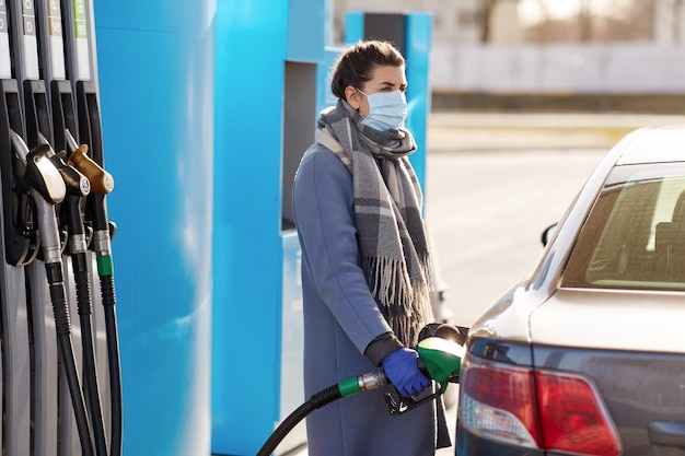 Une femme en masque remplissant sa voiture à la station-service.