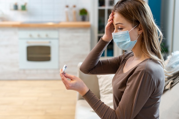 Photo femme avec masque restant en quarantaine vérifiant sa température